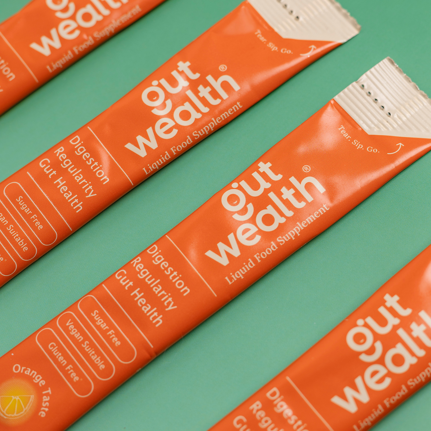Gut Wealth liquid food supplement sachets close-up on green background - sugar free vegan gluten free orange taste postbiotic for digestion and gut health