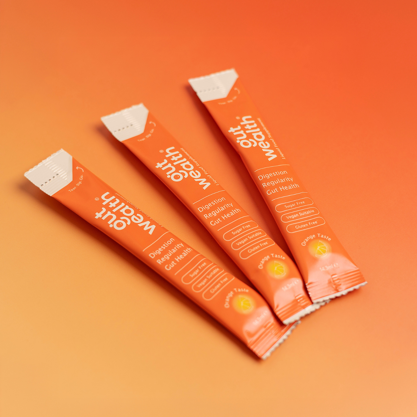 Three Gut Wealth liquid supplement sachets on orange background - postbiotic gut health sachets for digestion regularity and immune support